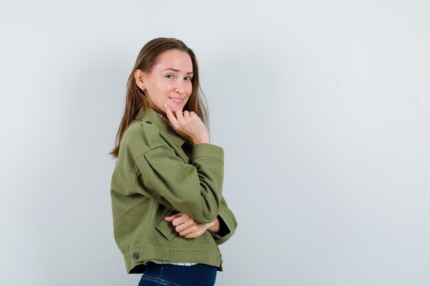 思考ポーズで立ってエレガントに見える緑のジャケットの若い女性。