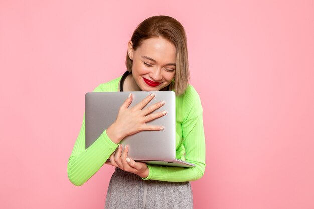 young woman in green shirt and grey skirt holding grey laptop with smile on her face