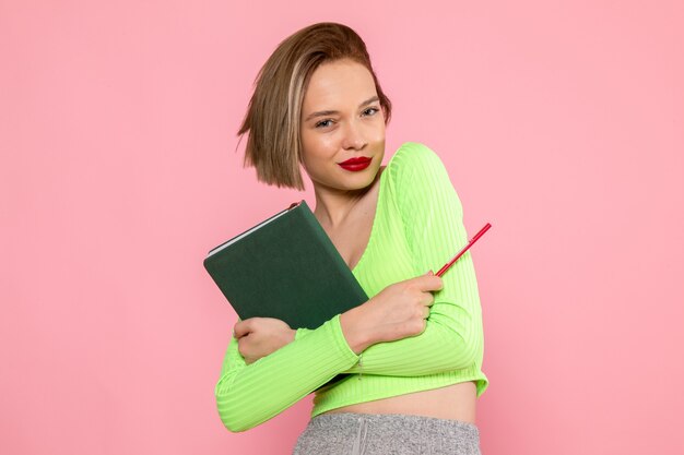 young woman in green shirt and grey skirt holding red pen and copybook