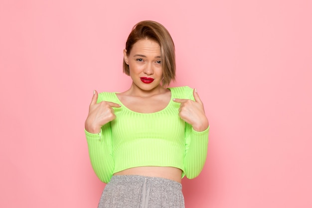 young woman in green shirt and grey skirt posing with confused expression