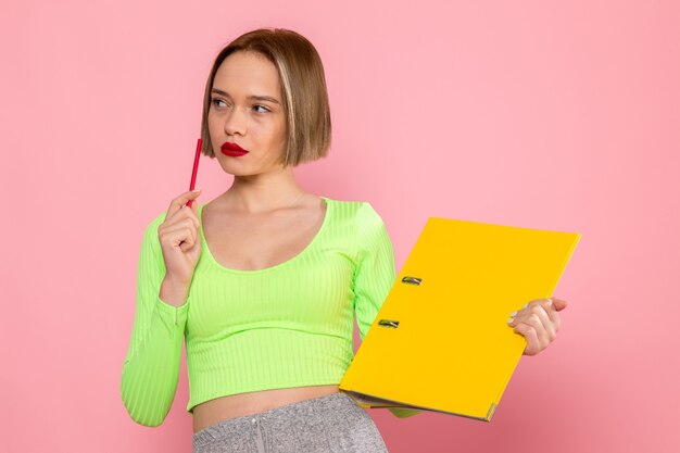 young woman in green shirt and grey skirt smiling holding red pen and yellow document