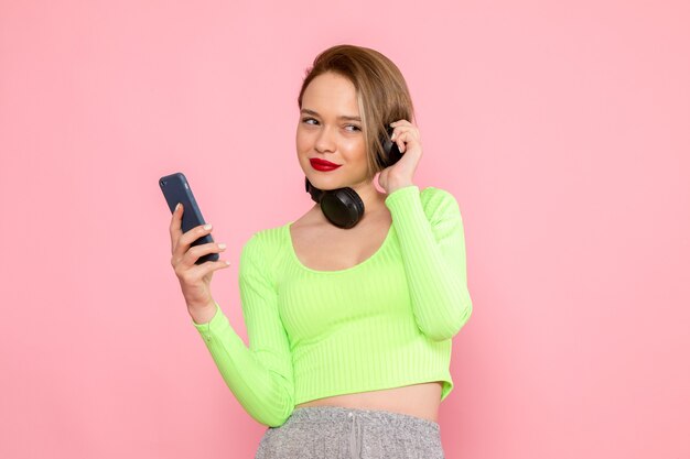 молодая женщина в зеленой рубашке и серой юбке разговаривает по телефону и слушает музыку