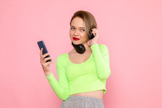 young woman in green shirt and grey skirt using a phone and listening to music