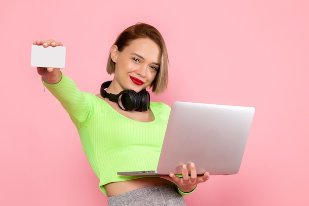 Free photo young woman in green shirt and grey trousers posing with laptop and black earphones