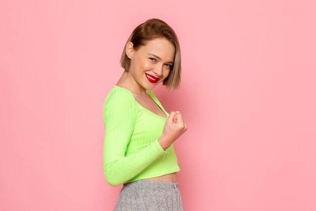 young woman in green shirt and grey trousers posing with smile on her face