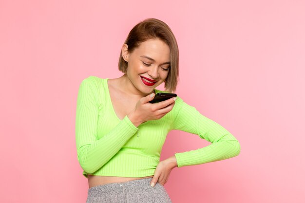 молодая женщина в зеленой рубашке и серых брюках улыбается и отправляет голосовое сообщение