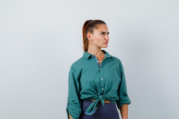 Young woman in green shirt looking away while frowning face, curving lips and looking pensive , front view.