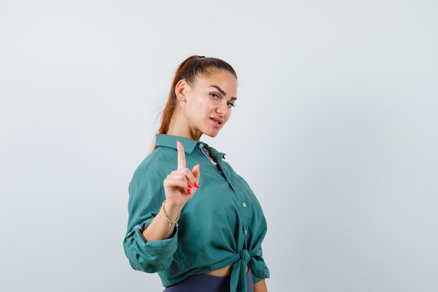 Free photo young woman in green shirt showing hold on a minute gesture and looking confident , front view.