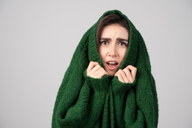 Young woman in green sweater looking shocked on gray.