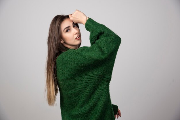 Giovane donna in maglione verde in posa su grigio.