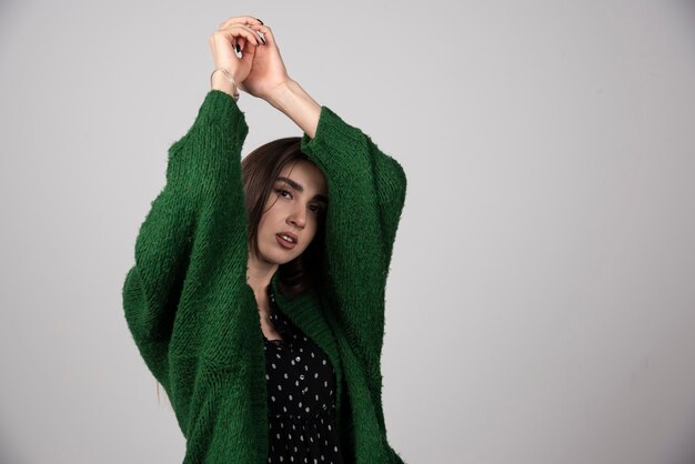 Молодая женщина в зеленом свитере позирует на сером.