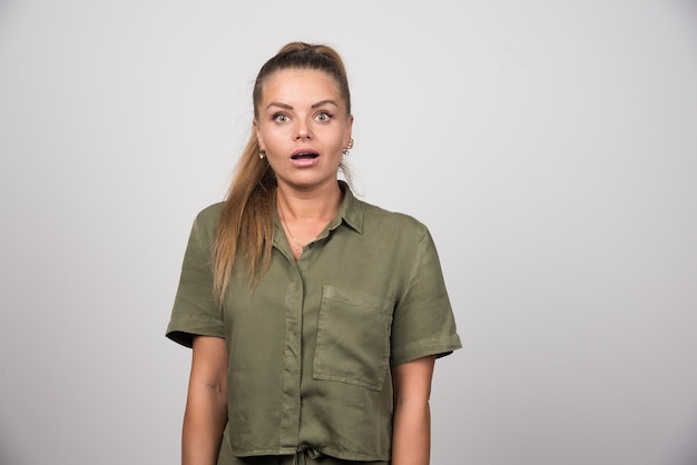 Young woman in green sweater standing on gray wall.