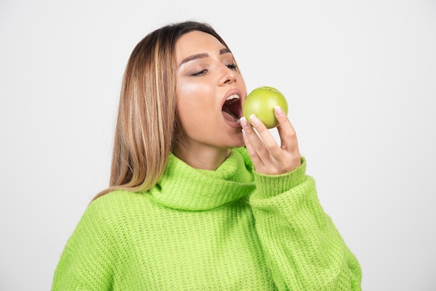 Foto gratuita giovane donna in maglietta verde che mangia una mela.