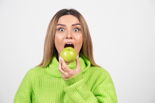 Молодая женщина в зеленой футболке ест яблоко.