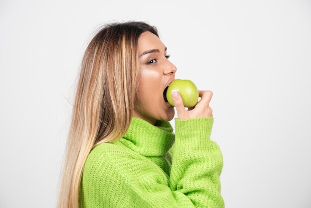 リンゴを食べる緑のTシャツの若い女性。