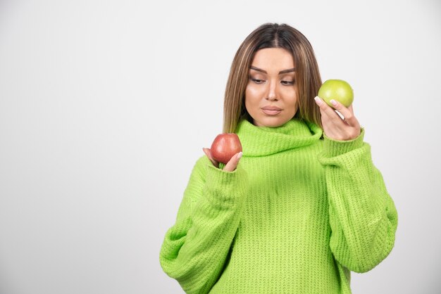 Young woman in green t-shirt holding two apples overhead.