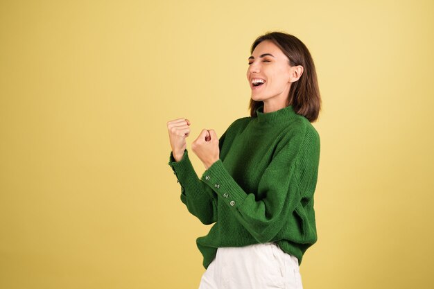 Молодая женщина в зеленом теплом свитере взволнована, показывая жест победителя
