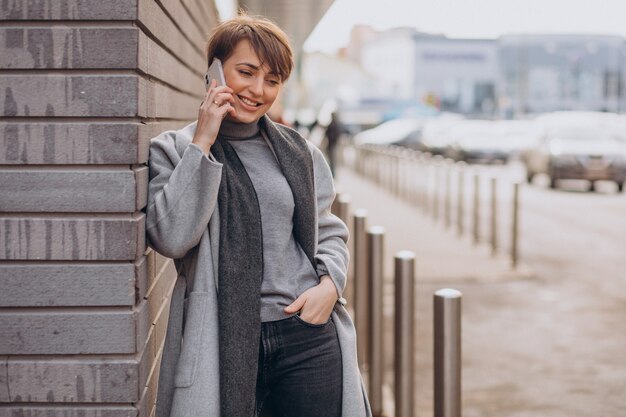 電話を使用して灰色のコートを着た若い女性