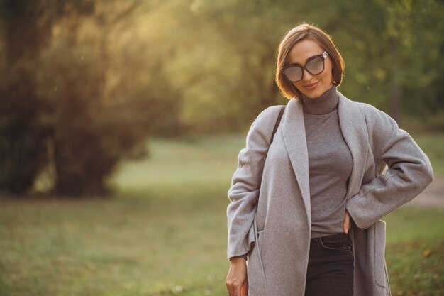 秋の公園を歩く灰色のコートを着た若い女性