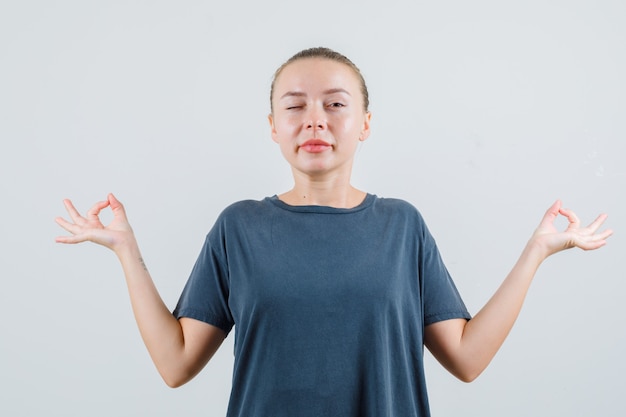 Foto gratuita giovane donna in maglietta grigia facendo meditazione e ammiccante