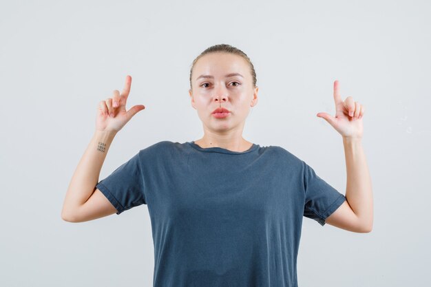 Young woman in grey t-shirt pointing up and looking careful