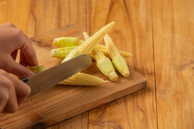 Young woman hand chopping corn on a chopping block.