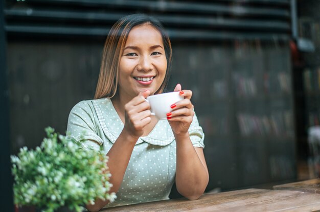 若い女性は喜んでカフェでコーヒーを飲みます