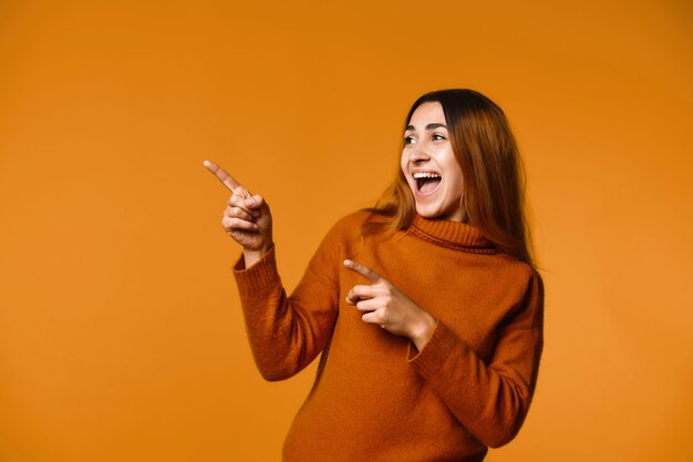 Young woman has joyful look and is pointing fingers aside standing