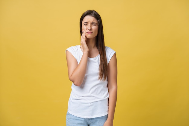 Young woman has a toothache studio photo isolated on a yellow background
