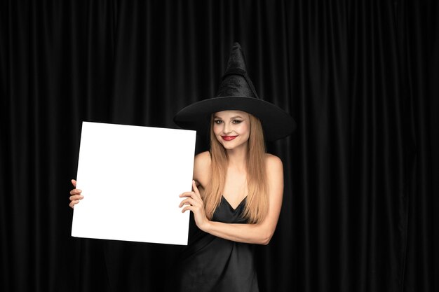 Young woman in hat as a witch on black curtain