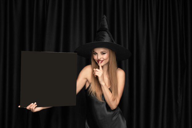 Young woman in hat as a witch on black curtain