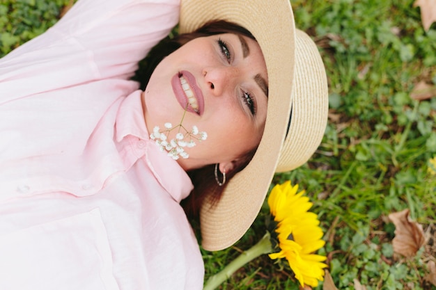 笑みを浮かべて、草の上に横たわる帽子の若い女