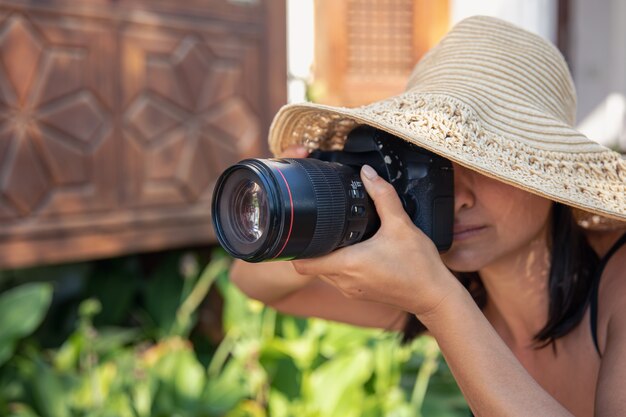 A young woman in a hat takes pictures with a professional SLR camera on a hot summer day.