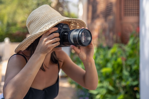 모자를 쓴 젊은 여성이 더운 여름날 전문 SLR 카메라로 사진을 찍습니다.