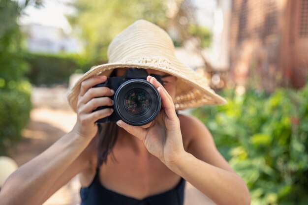 A young woman in a hat takes pictures with a professional SLR camera on a hot summer day