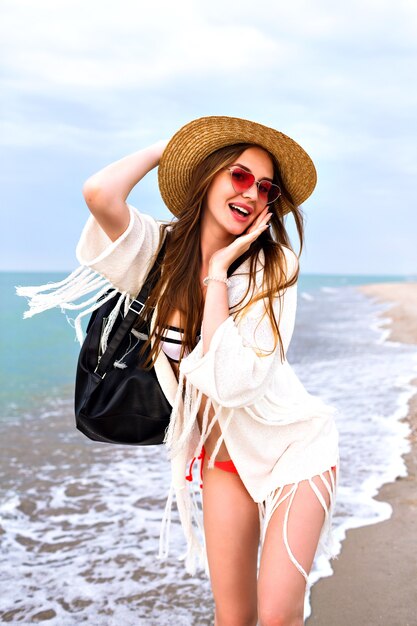 Young woman having fun in lonely beach, enjoy summer vacation and relax, boho outfit, straw hat and bikini