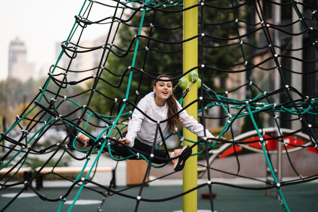 Young woman having fun on the rope pyramid on the playground