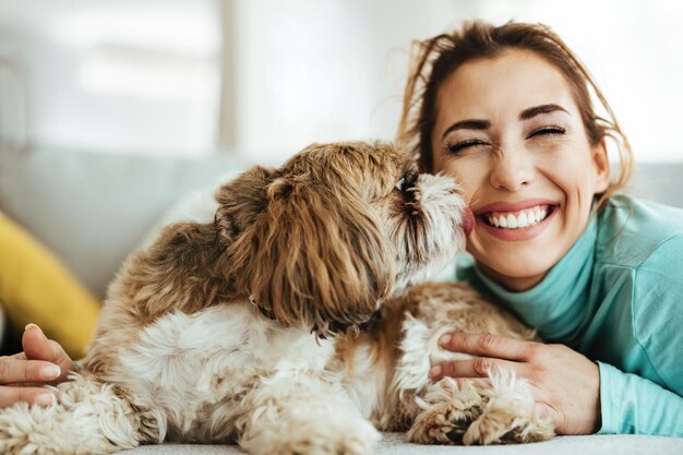 Young woman having fun while her dog is kissing her at home