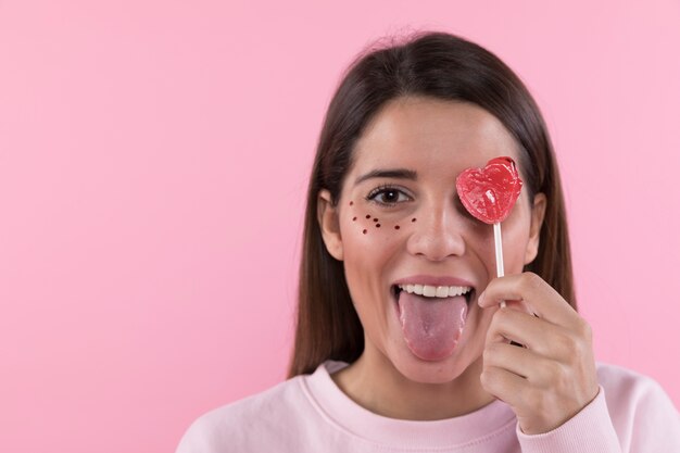 Young woman having fun with ornament glitters on face and lollipop