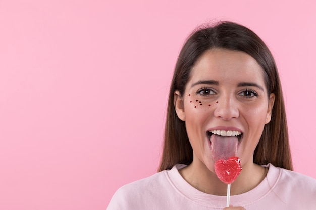 Free photo young woman having fun with ornament glitters on face and sweet candy