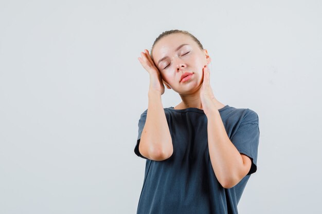 Young woman having headache and rubbing temples in grey t-shirt and looking tired