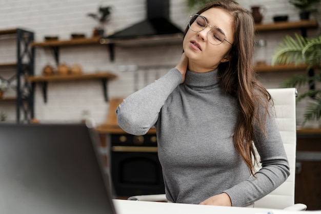 Free photo young woman having a neckache while working from home
