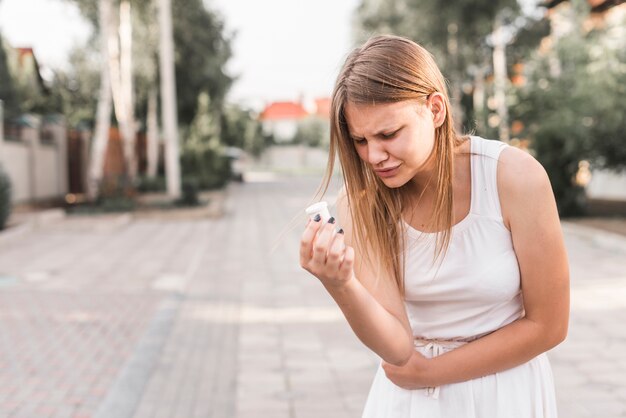 Young woman having stomach ache holding white pills bottle