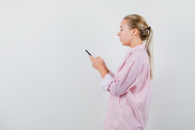 Young woman having text chat on mobile phone in pink shirt