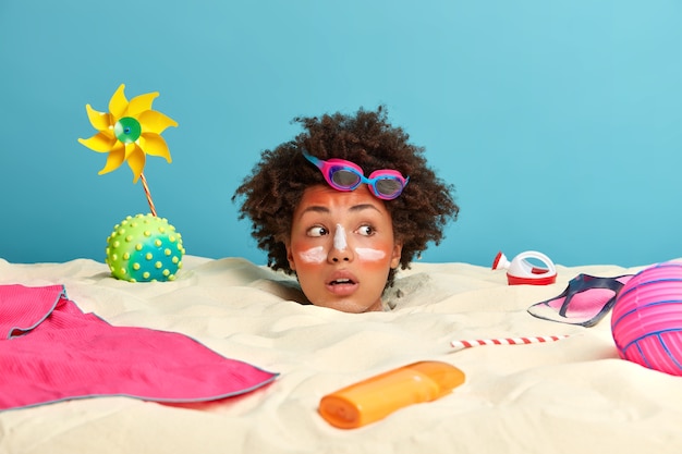 Young woman head with sunscreen cream on face surrounded by beach accessories