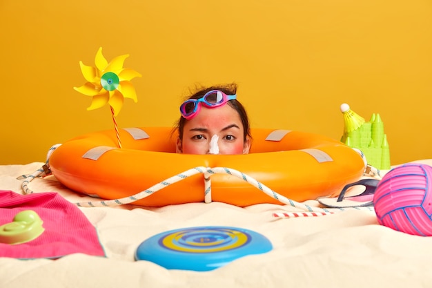 Young woman head with sunscreen cream on face surrounded by beach accessories