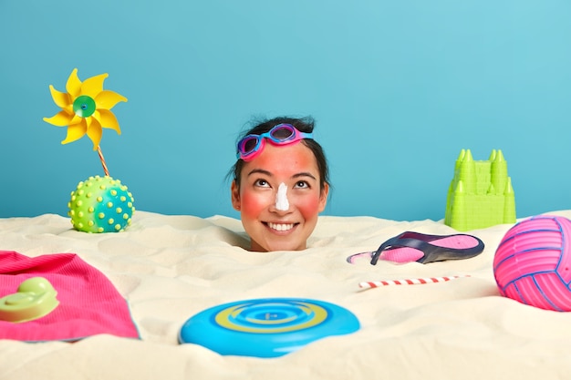 Foto gratuita testa di giovane donna con crema solare sul viso circondato da accessori da spiaggia