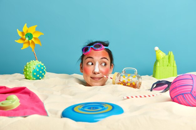 Young woman head with sunscreen cream on face surrounded by beach accessories