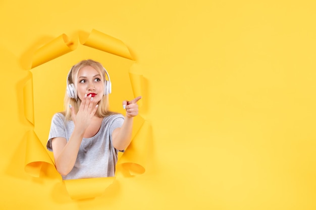 Free photo young woman in headphones pointing at something on yellow surface