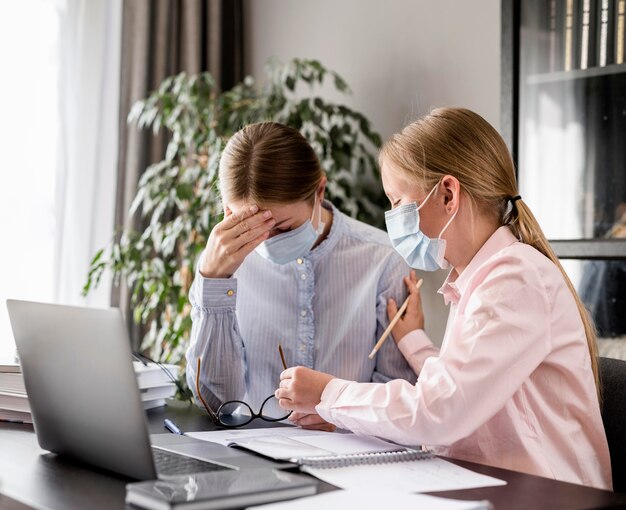 Young woman helping girl with homework while wearing a medical mask